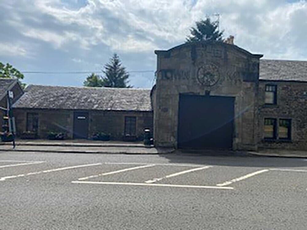 A historic stone building with a large archway entrance on a cloudy day. The street in front has empty parking spaces. - Home Instead