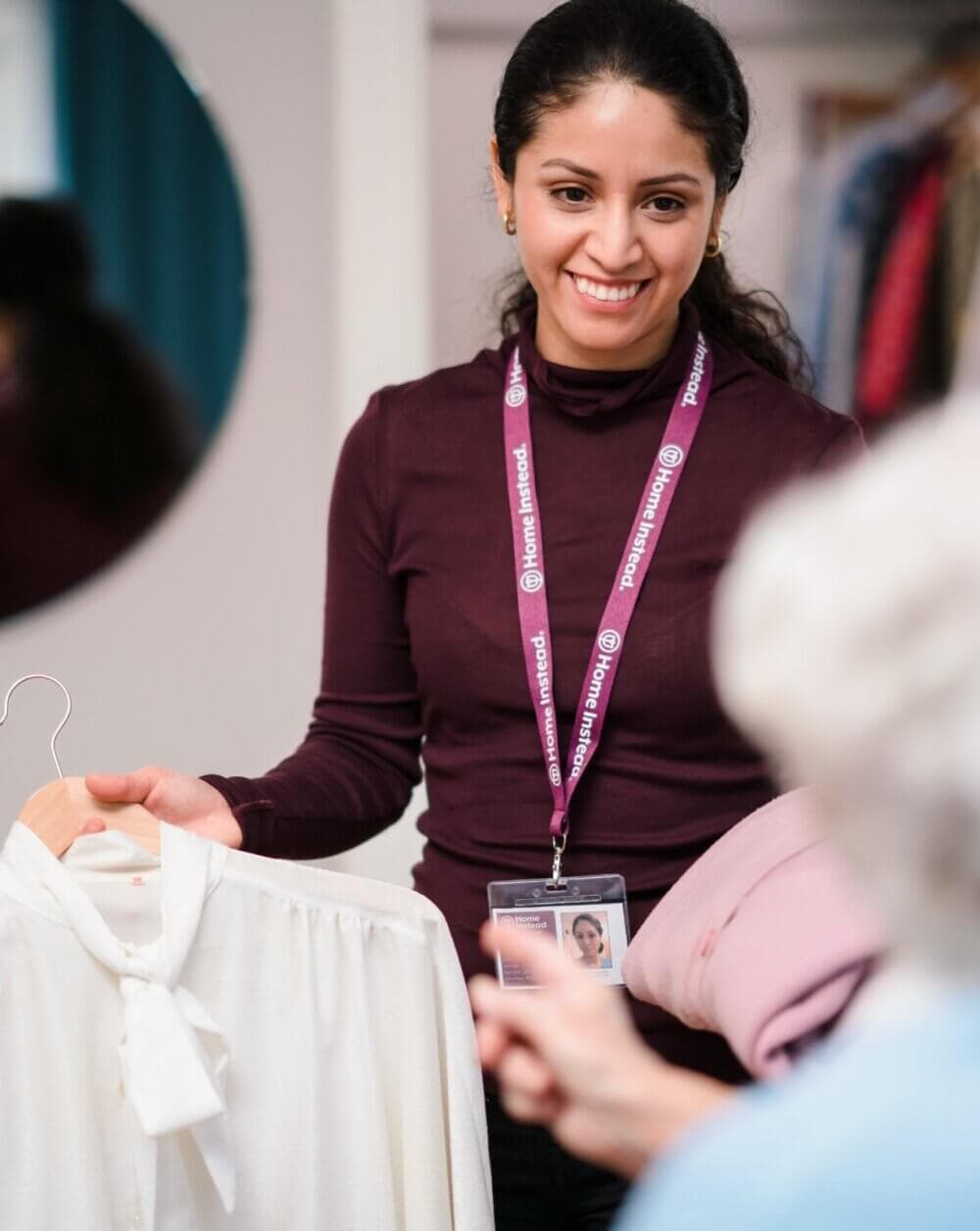 A smiling woman shows a white blouse to a customer in a clothing store. - Home Instead