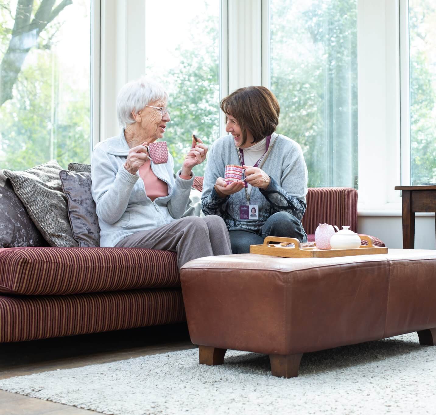 An elderly woman and a younger woman having tea and sitting on a couch by a window in a well-lit room. - Home Instead Poole