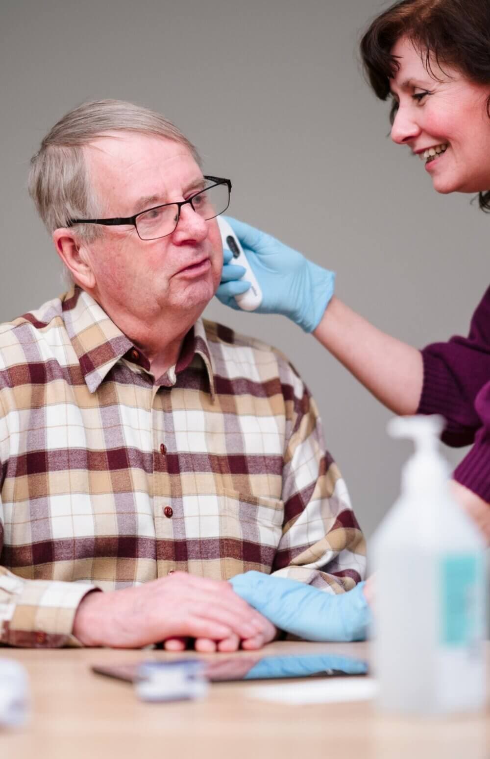 A healthcare professional checks the ear of an elderly man with a device. Both are smiling. - Home Instead