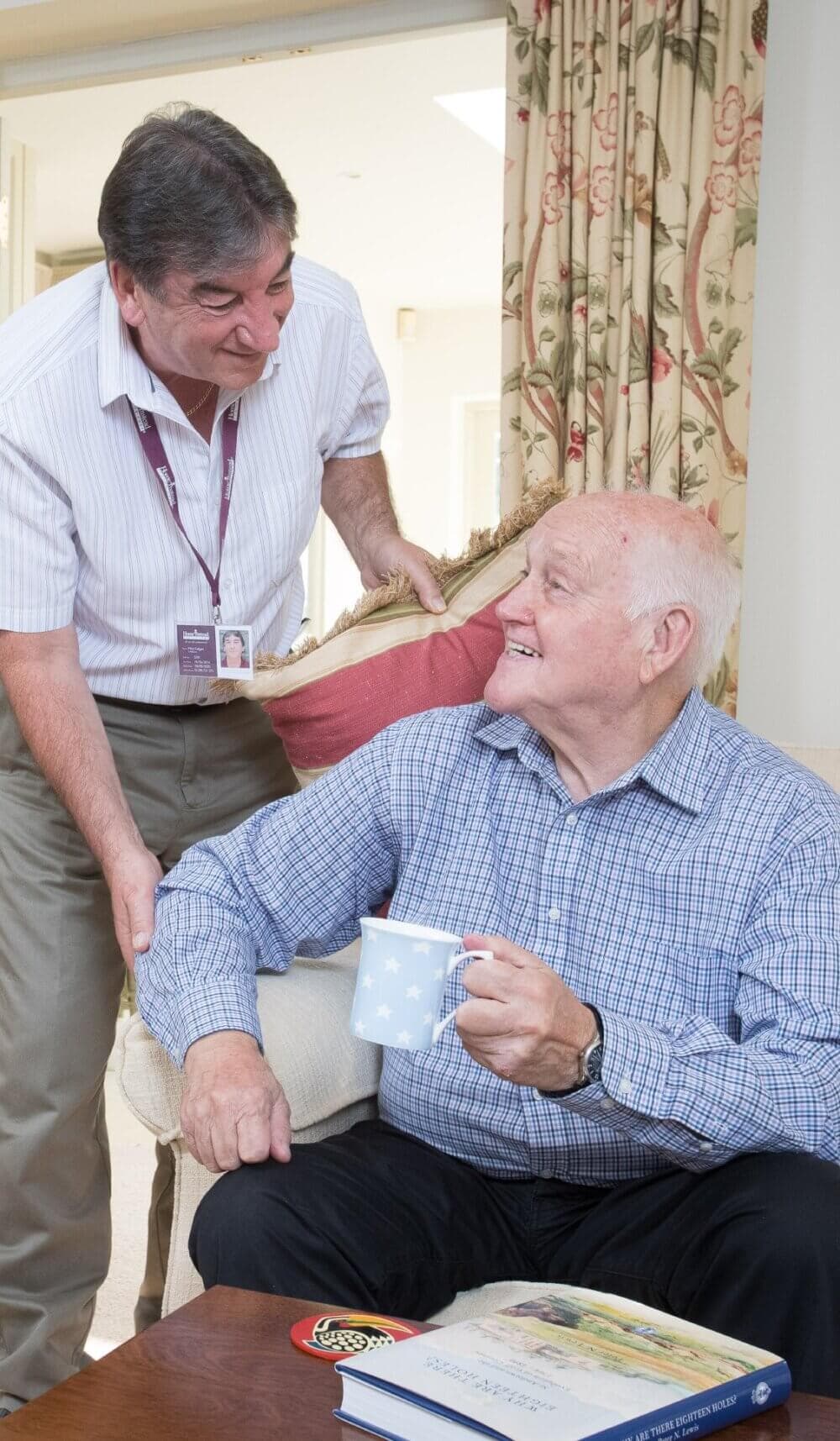Elderly woman with white hair, blue cardigan, and glasses, smiling while holding a cookie and sitting on a couch. - Home Instead Poole