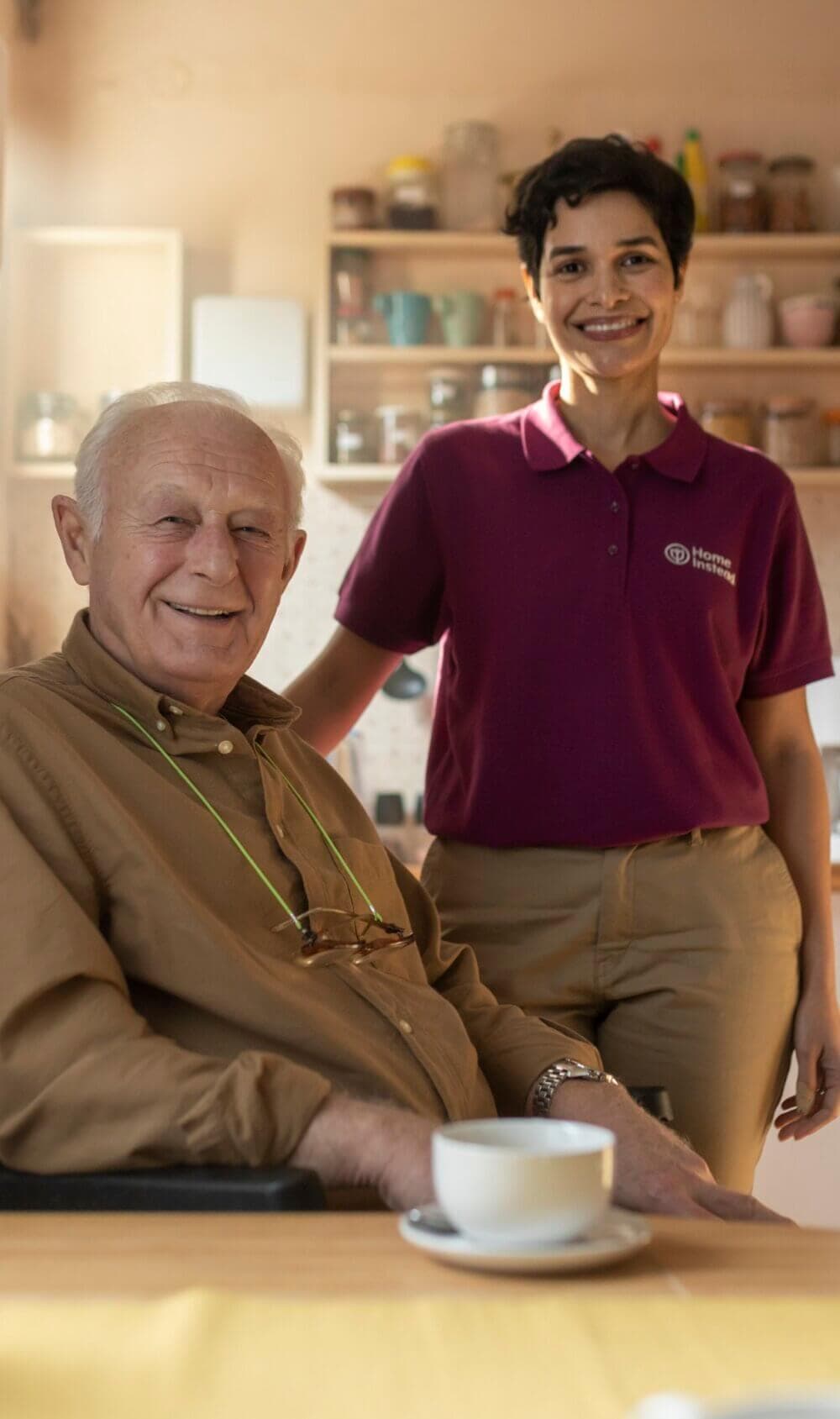 Elderly woman with white hair, in a light blue cardigan, smiling while seated on a sofa and holding a cookie. - Home Instead