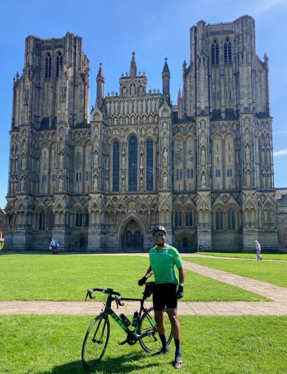 Cyclist in green outfit standing with bike in front of a large cathedral on a clear day. - Home Instead