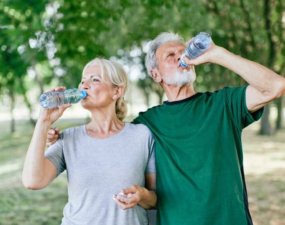 Two elderly people in a park, drinking bottled water and wearing casual clothes. - Home Instead Bournemouth & Christchurch