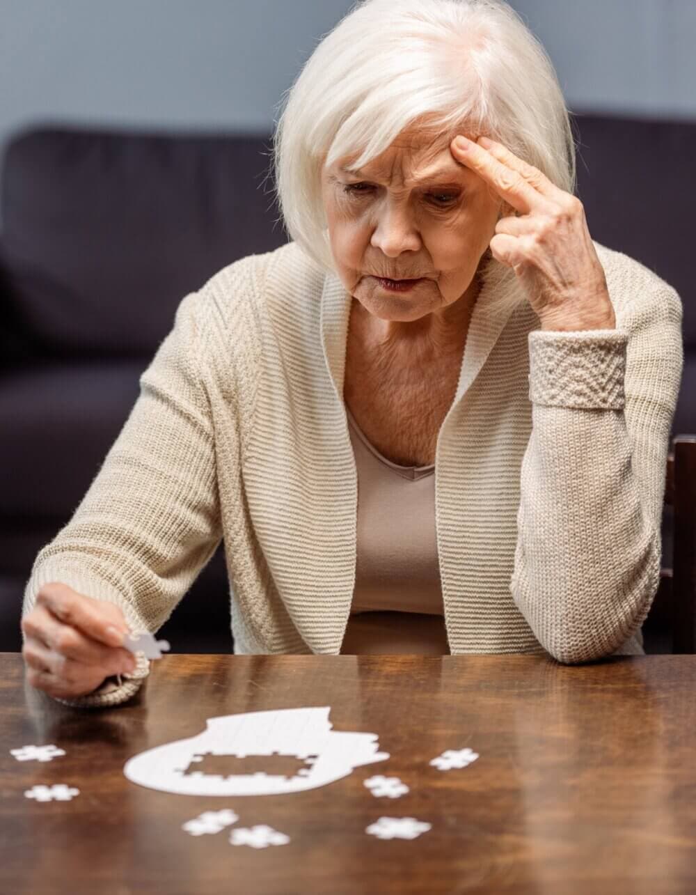 Elderly woman concentrating on completing a puzzle at a table. - Home Instead