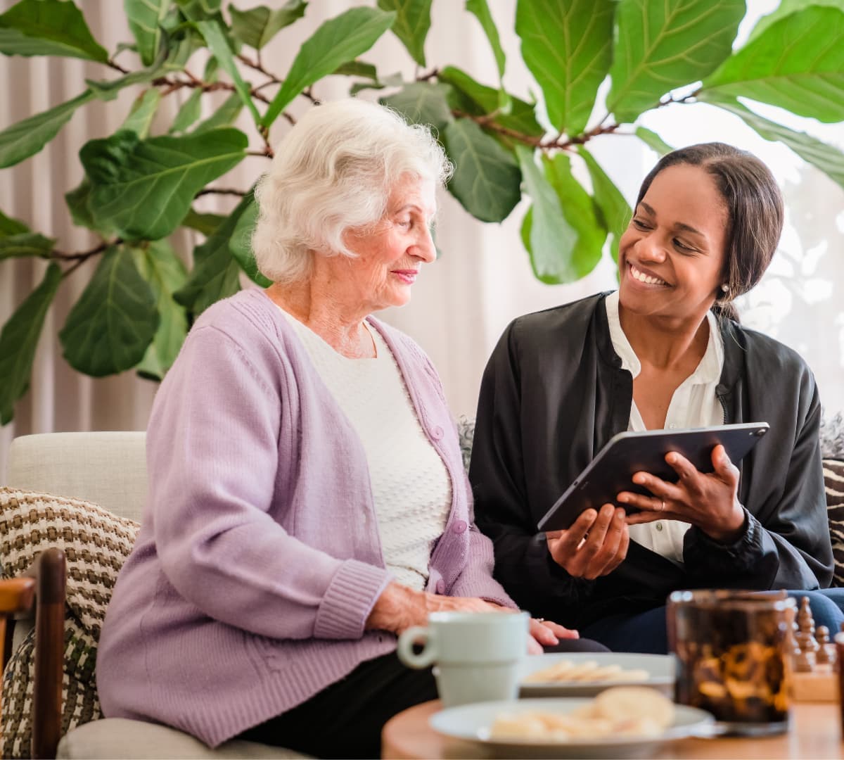 Client using tablet and smiling with Home Instead Southampton Care Professional