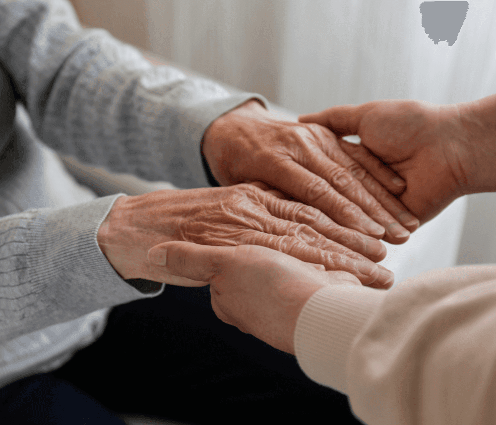 A younger person holds the hands of an older person, offering comfort and support. - Home Instead