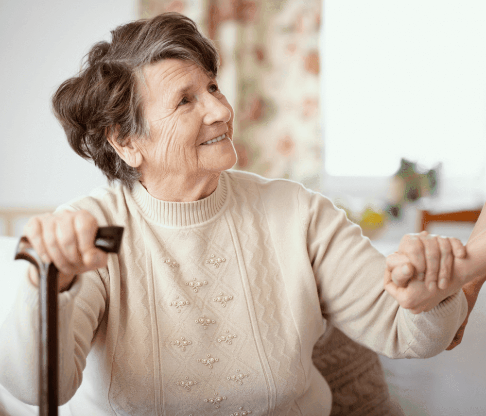 Smiling elderly woman with short hair holding a cane and reaching out to hold someone's hand. - Home Instead