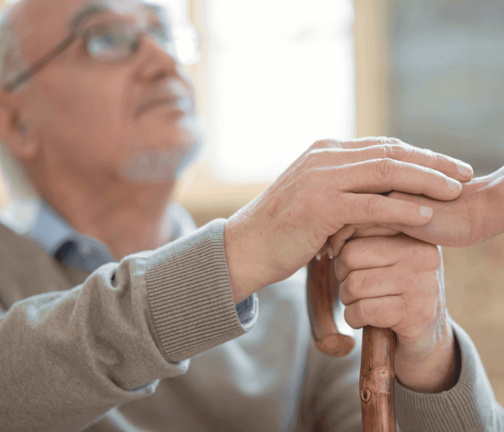 Elderly man holding a walking cane, looking up with a thoughtful expression. - Home Instead
