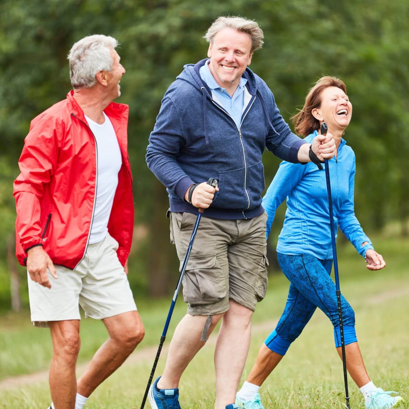 Three happy people walking outdoors with Nordic walking poles on a green path. - Home Instead