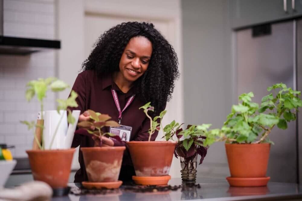 A woman smiles while tending to potted plants on a kitchen countertop. - Home Instead