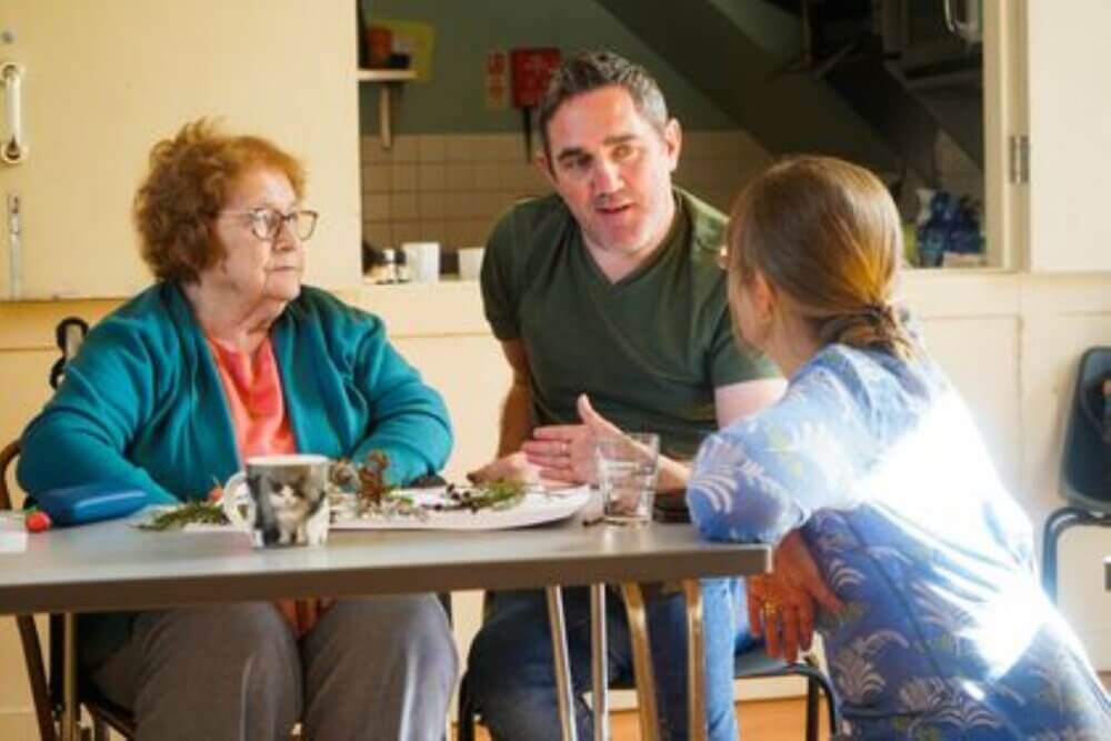 Three people seated at a table having a conversation with items spread out on the table. - Home Instead