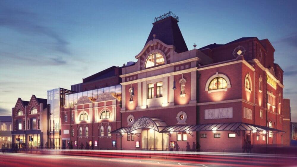 A warmly lit theater building with a large arched entrance, ornate windows, and a sign reading "Palace" at dusk. - Home Instead