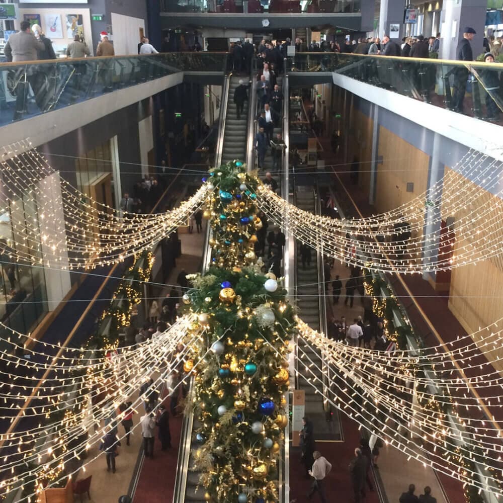 Indoor mall decorated with holiday lights, ornaments, and garlands; people using escalators and walking around. - Home Instead