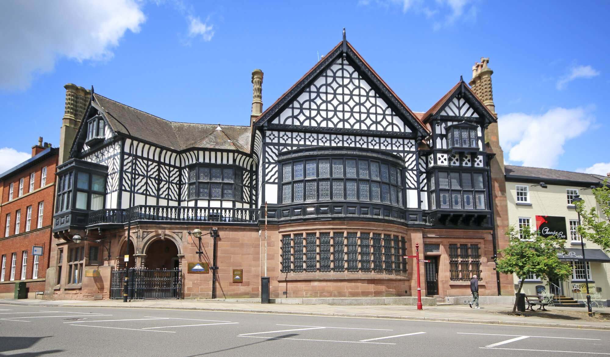 Historic black and white Tudor-style building with arched entrance, bay windows, and chimneys on a sunny day. - Home Instead