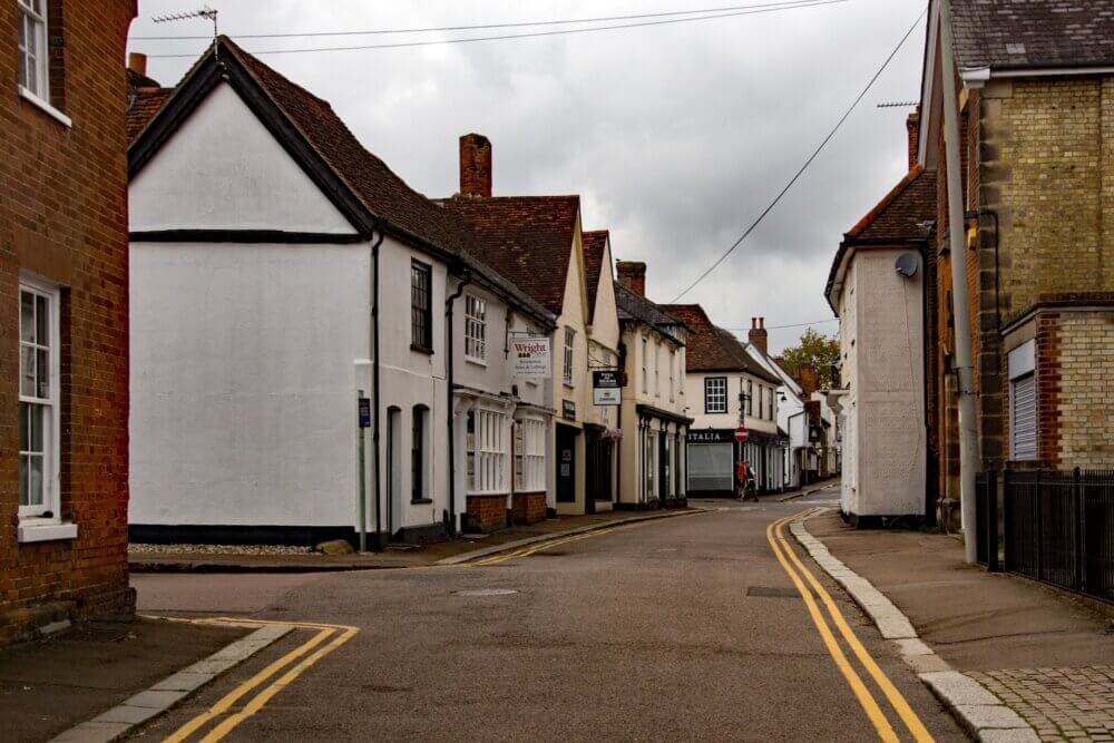 A narrow, empty street with old, white-painted buildings under a cloudy sky in a small town. - Home Instead