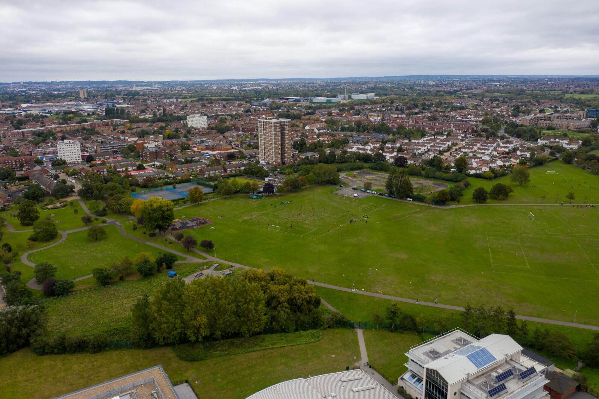 Aerial view of a green park area with sports fields, surrounded by residential buildings and trees under a cloudy sky. - Home Instead