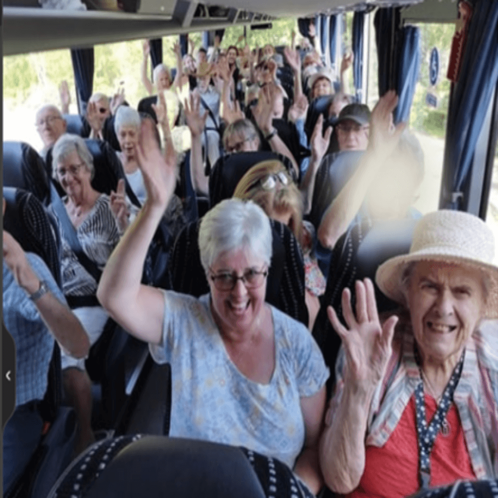A group of elderly people smiling and waving while sitting inside a bus. - Home Instead