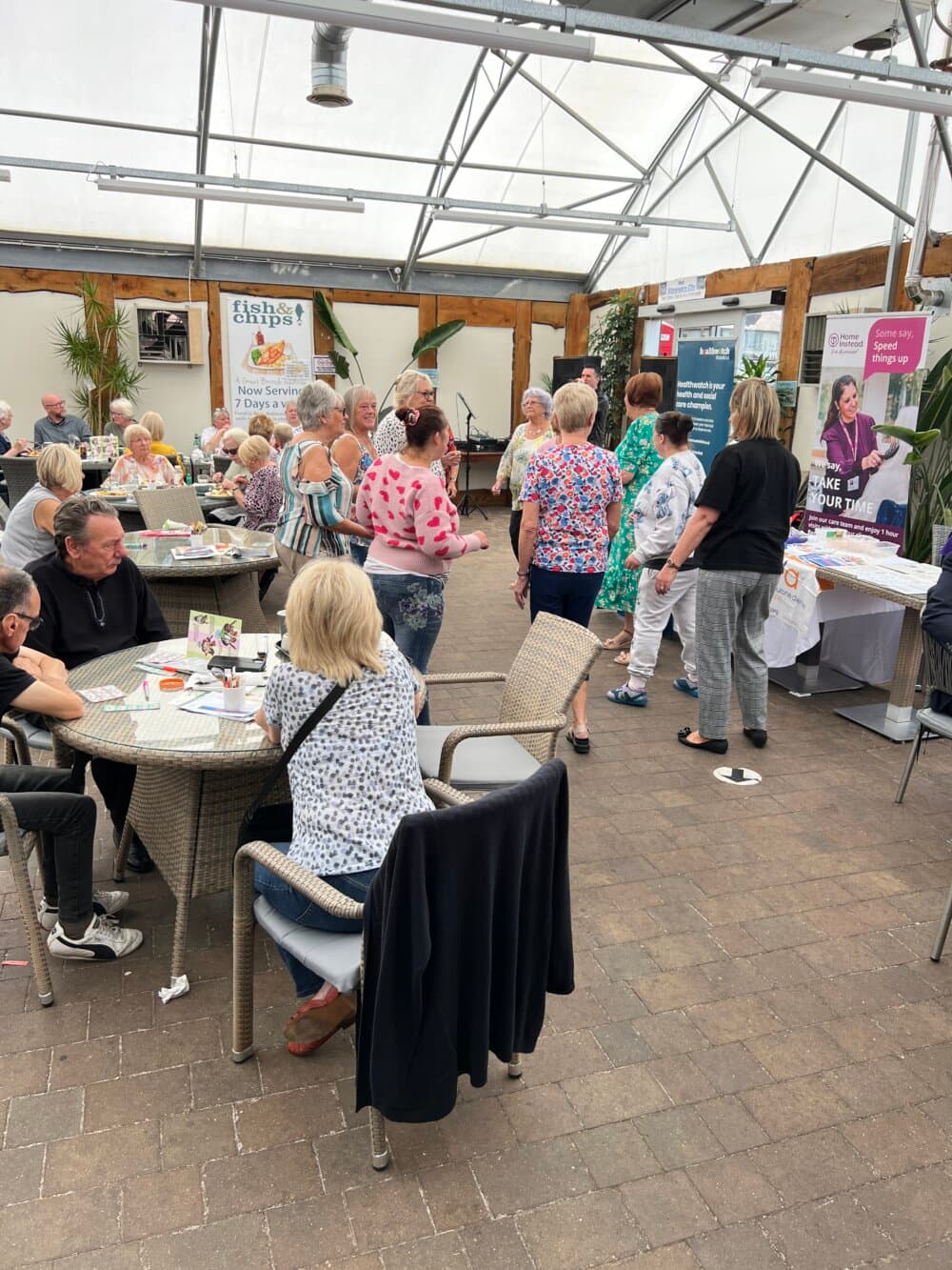 A group of people socializing and visiting booths at an indoor event with tables and informational stands. - Home Instead