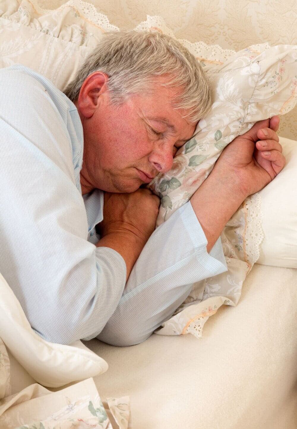 An elderly man with gray hair is sleeping peacefully on a pillow in a cozy bed. - Home Instead