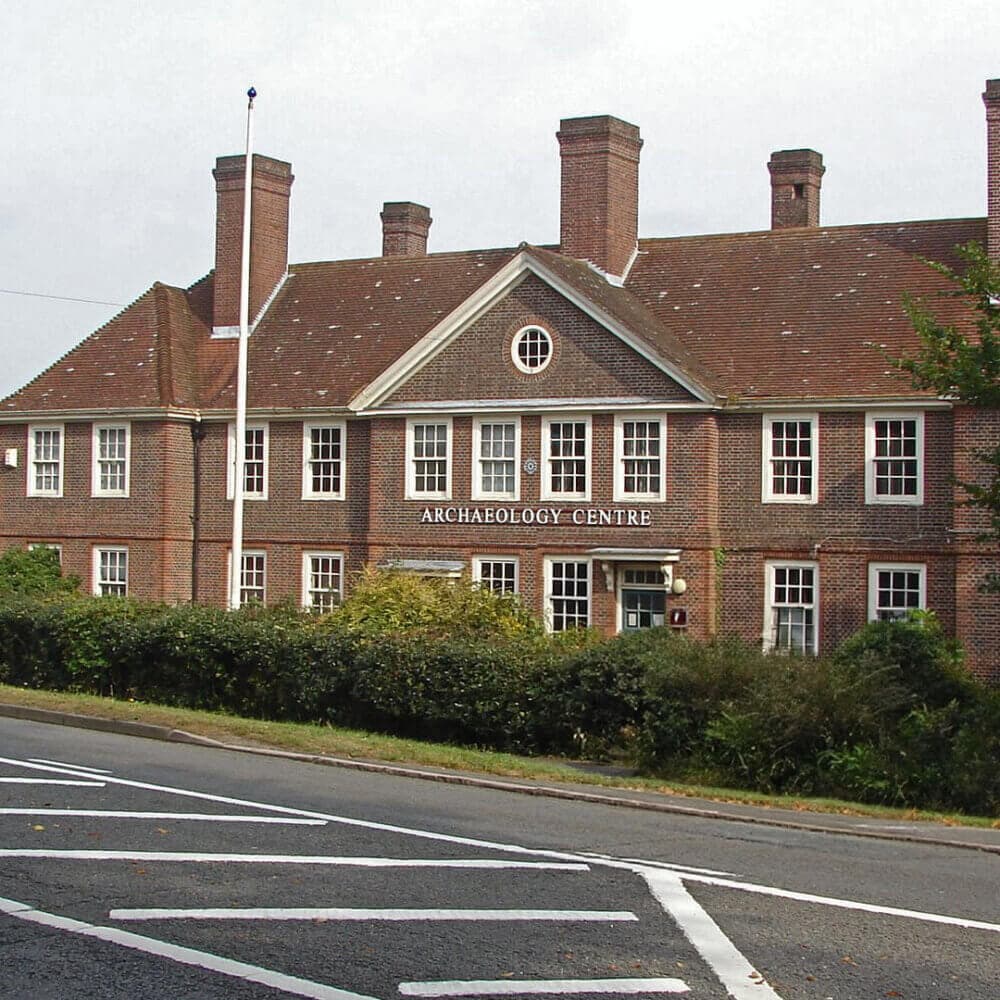 A two-story red-brick building labeled "Archaeology Centre" with multiple windows and a sloped roof. - Home Instead