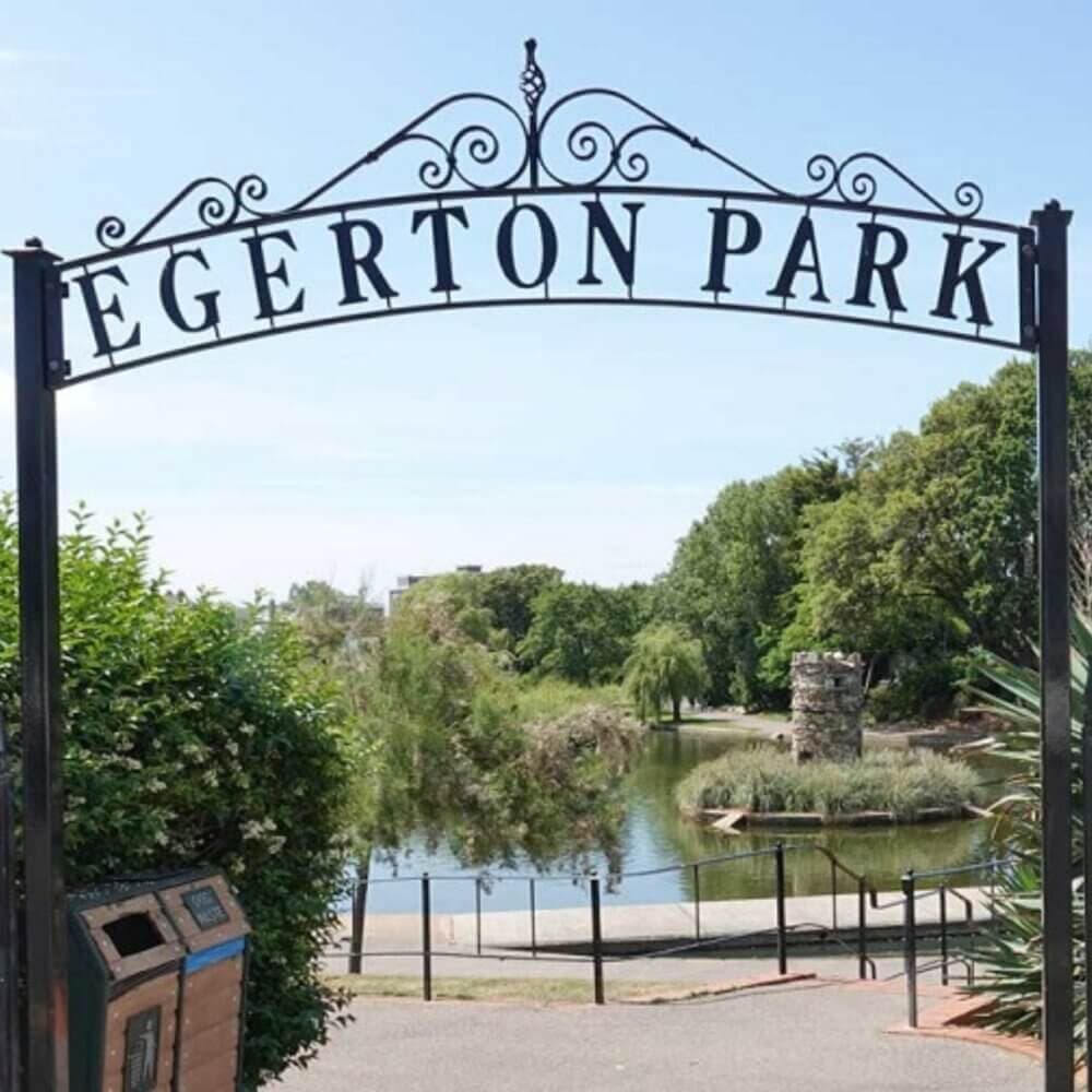 Entrance sign for Egerton Park with a view of a pond and lush greenery in the background on a sunny day. - Home Instead