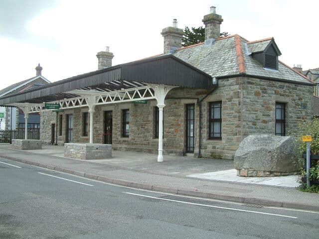 A traditional stone train station building with a canopy over the platform, adjacent to a quiet roadway. - Home Instead