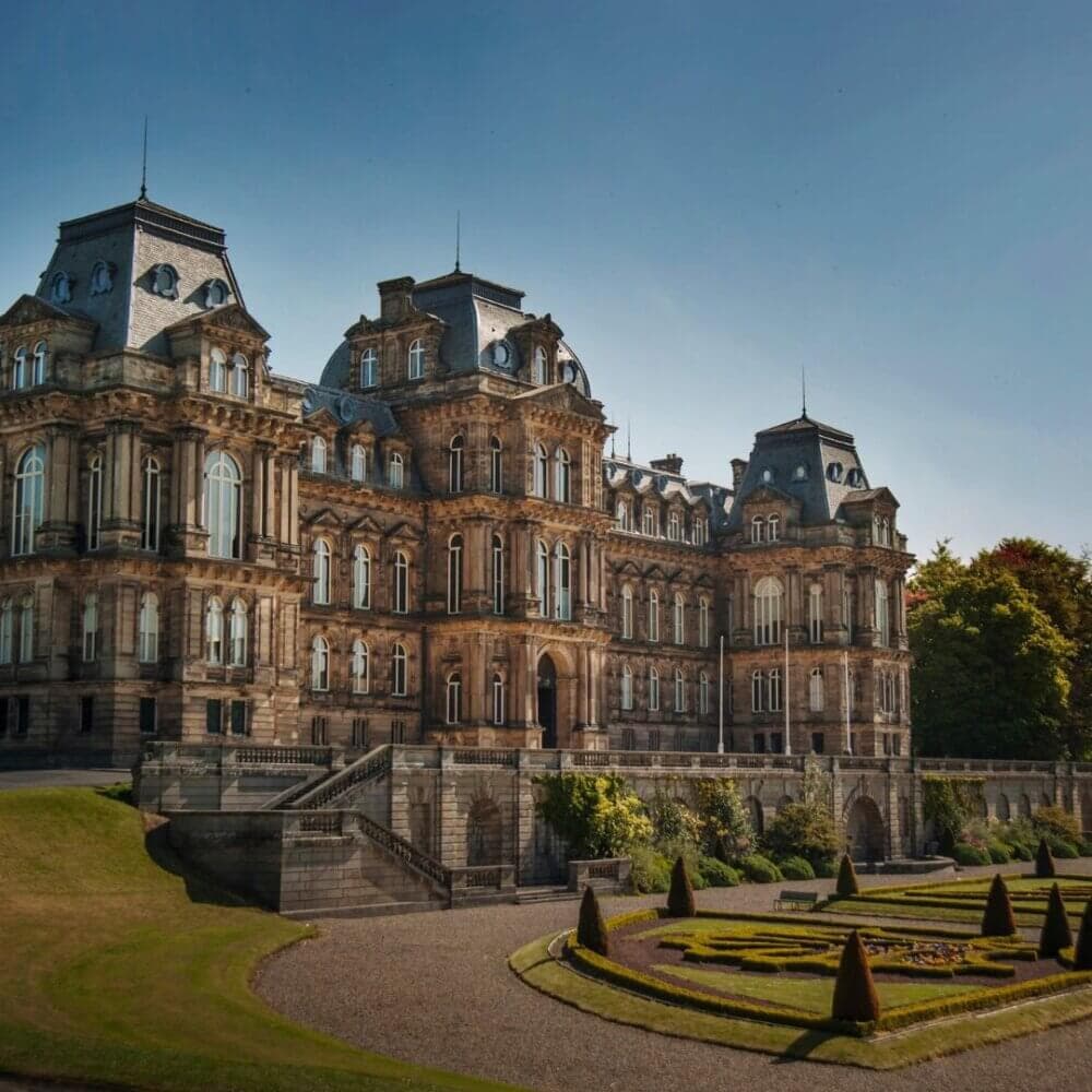 A majestic historic building with elaborate architecture and manicured gardens under a clear sky. - Home Instead