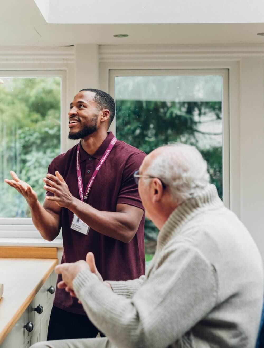 A Care Professional with an elderly client in a sweater, both inside a bright room with large windows. - Home Instead Bournemouth & Christchurch
