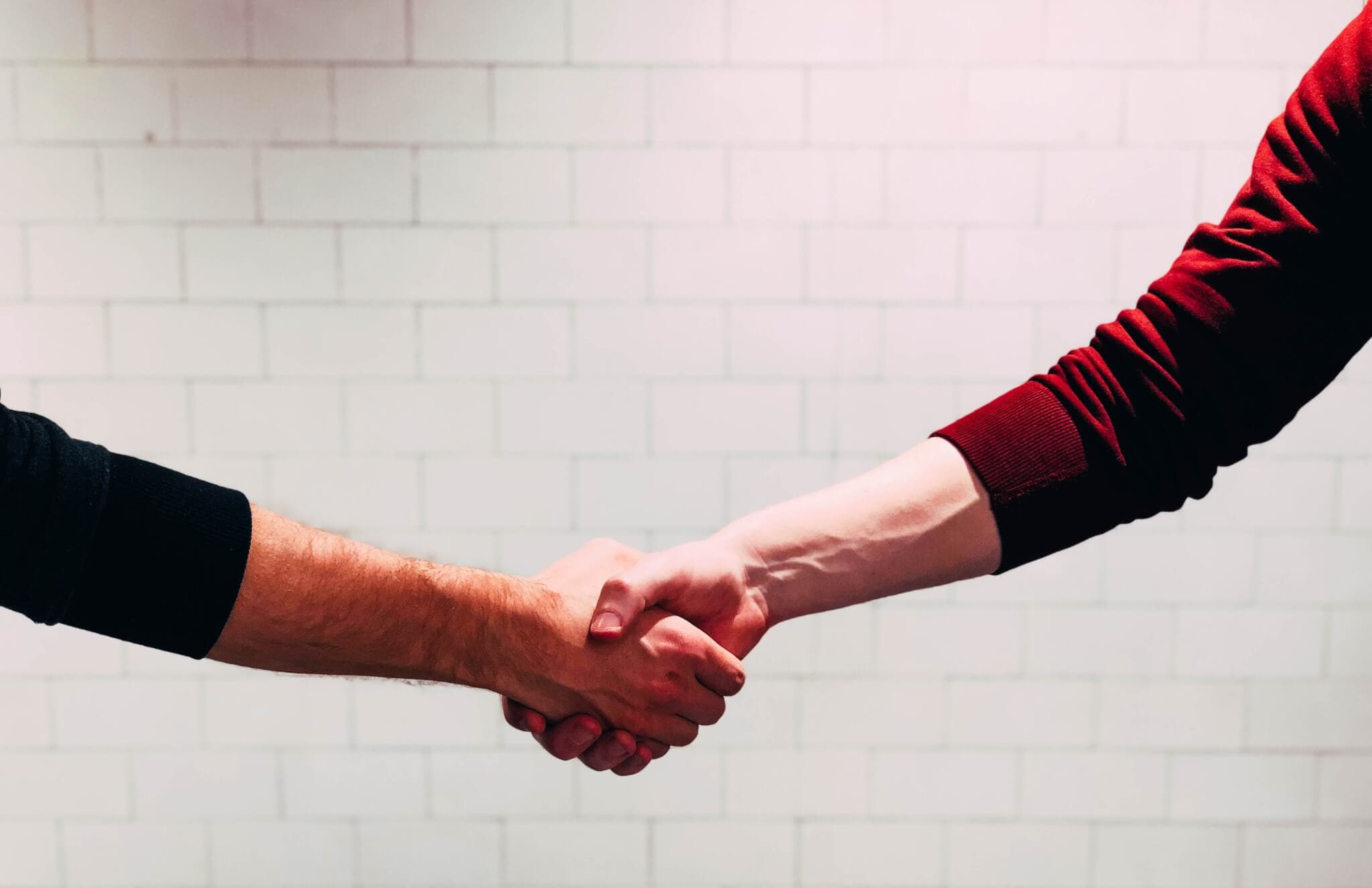 Two people shaking hands in front of a white brick wall, symbolizing agreement or partnership. - Home Instead