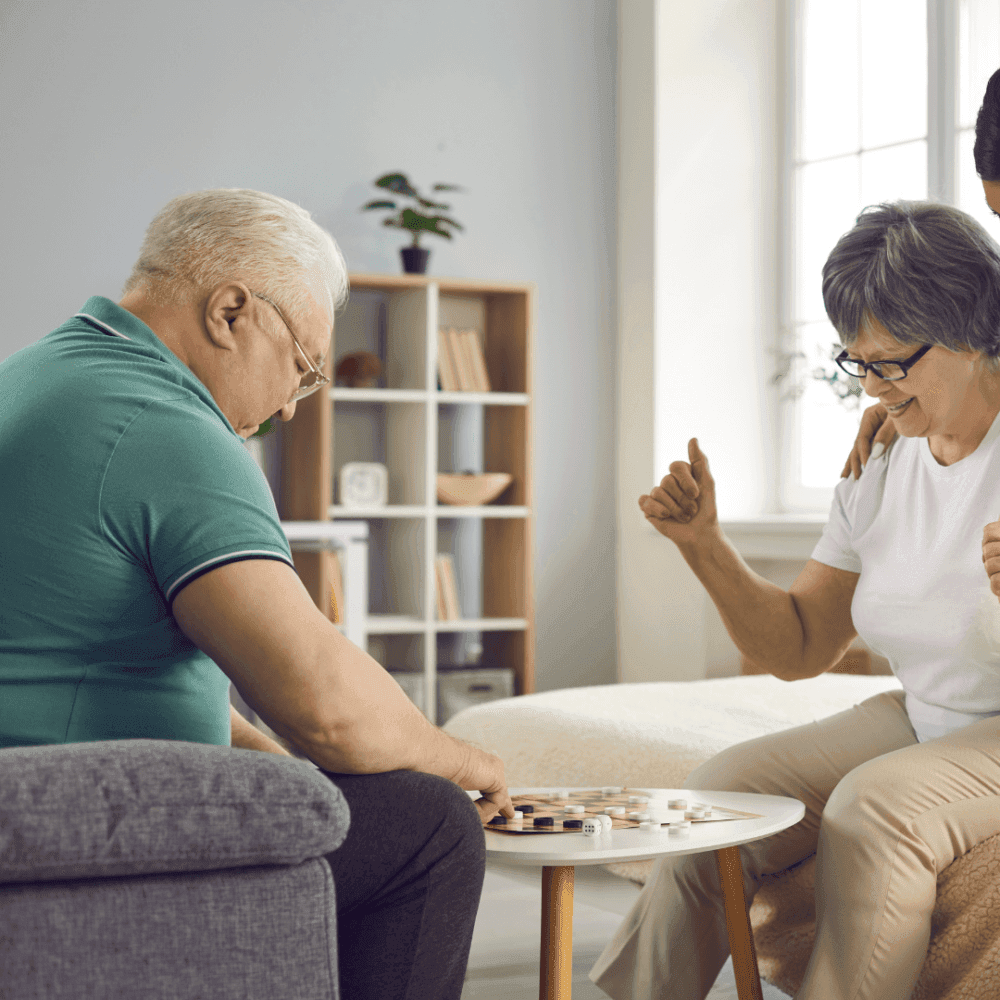 Two elderly people playing a game together at a table, smiling, and appearing joyful. - Home Instead