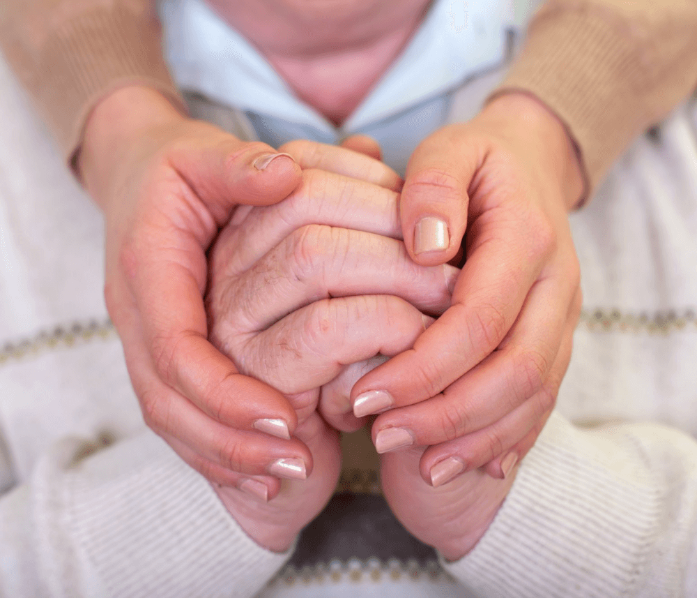 Two pairs of hands, one elderly and one younger, are clasped together gently, symbolizing care and support. - Home Instead