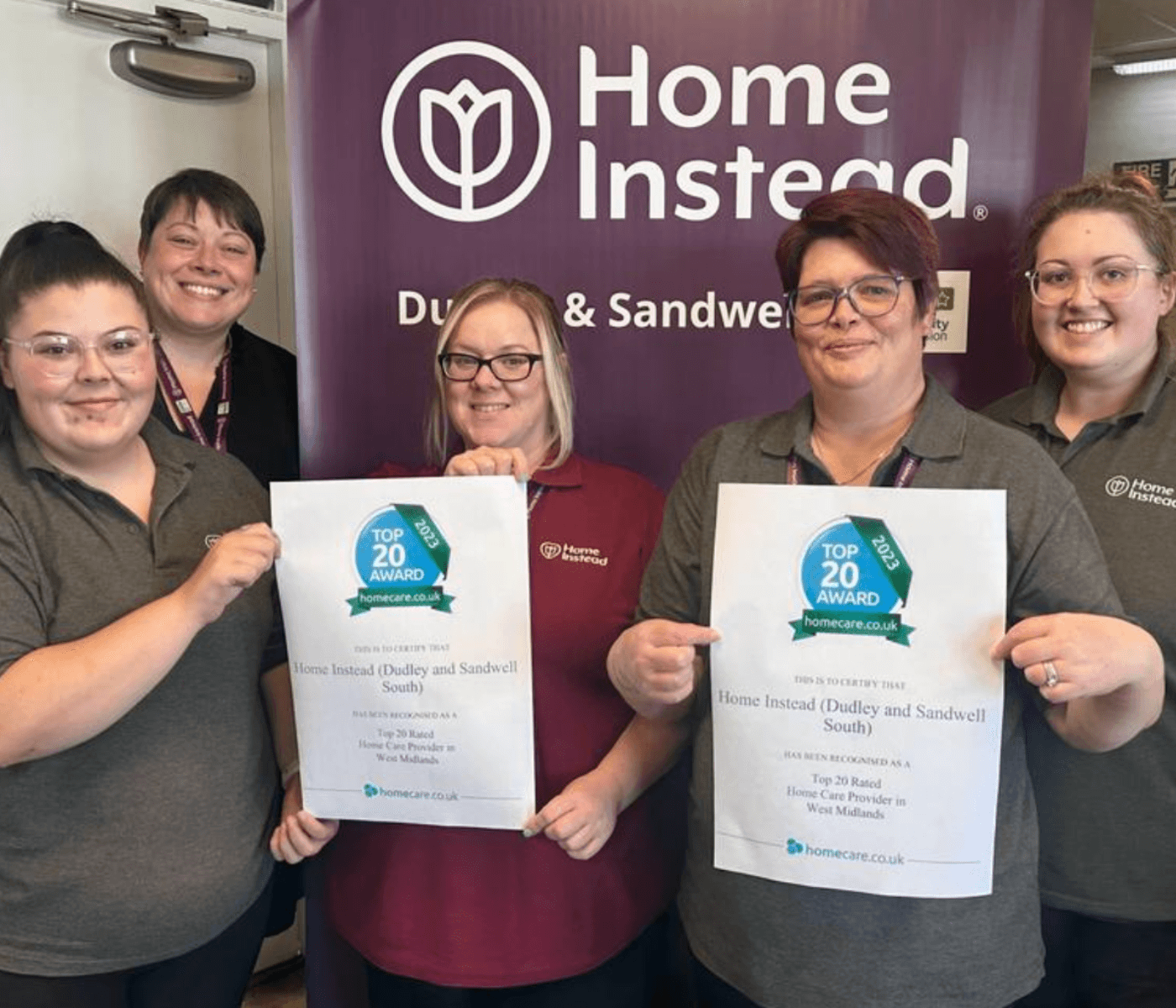 Five smiling individuals holding award certificates, standing in front of a "Home Instead Dudley & Sandwell South" banner. - Home Instead