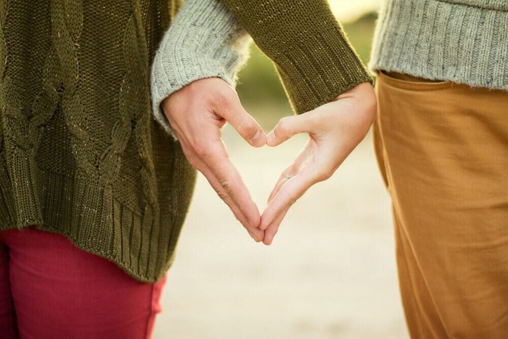 Two people in sweaters form a heart shape with their hands, symbolizing love and connection. - Home Instead