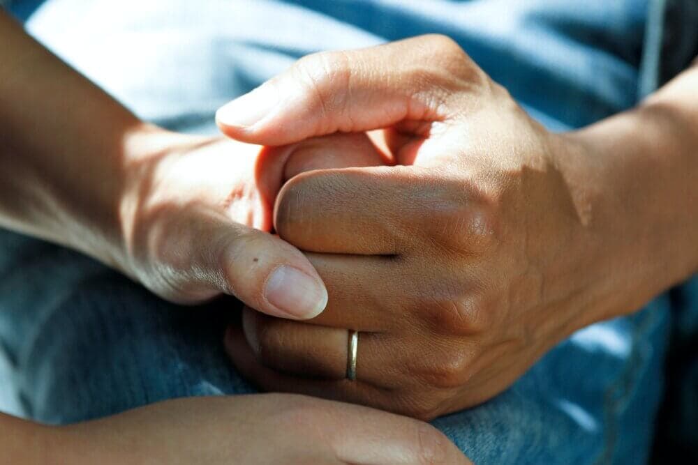 Two hands gently holding each other, one with a wedding ring, conveying support and comfort. - Home Instead