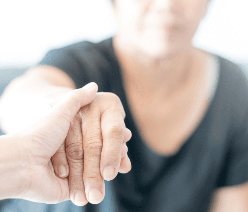 A close-up of one person gently holding the hand of another, creating a sense of comfort and support. - Home Instead