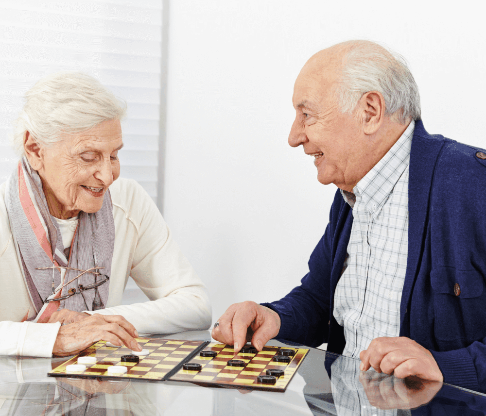 Elderly man and woman playing checkers and smiling at each other. - Home Instead