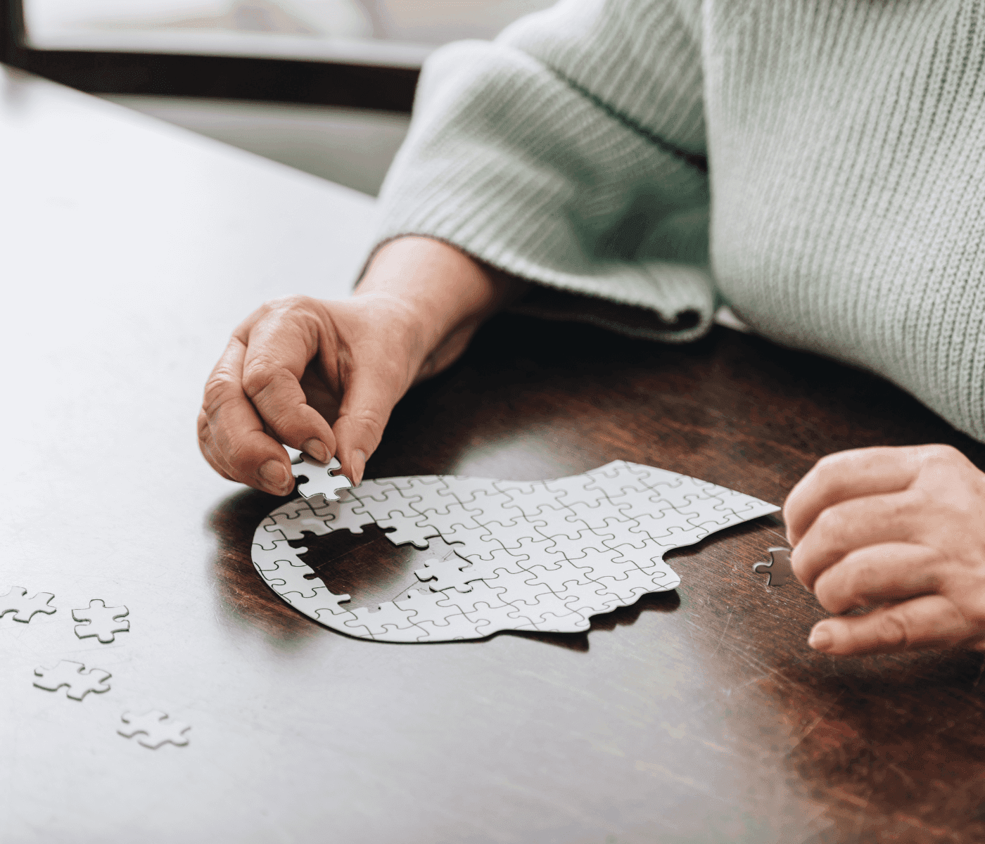 Person assembling a jigsaw puzzle shaped like a human head on a wooden table. - Home Instead