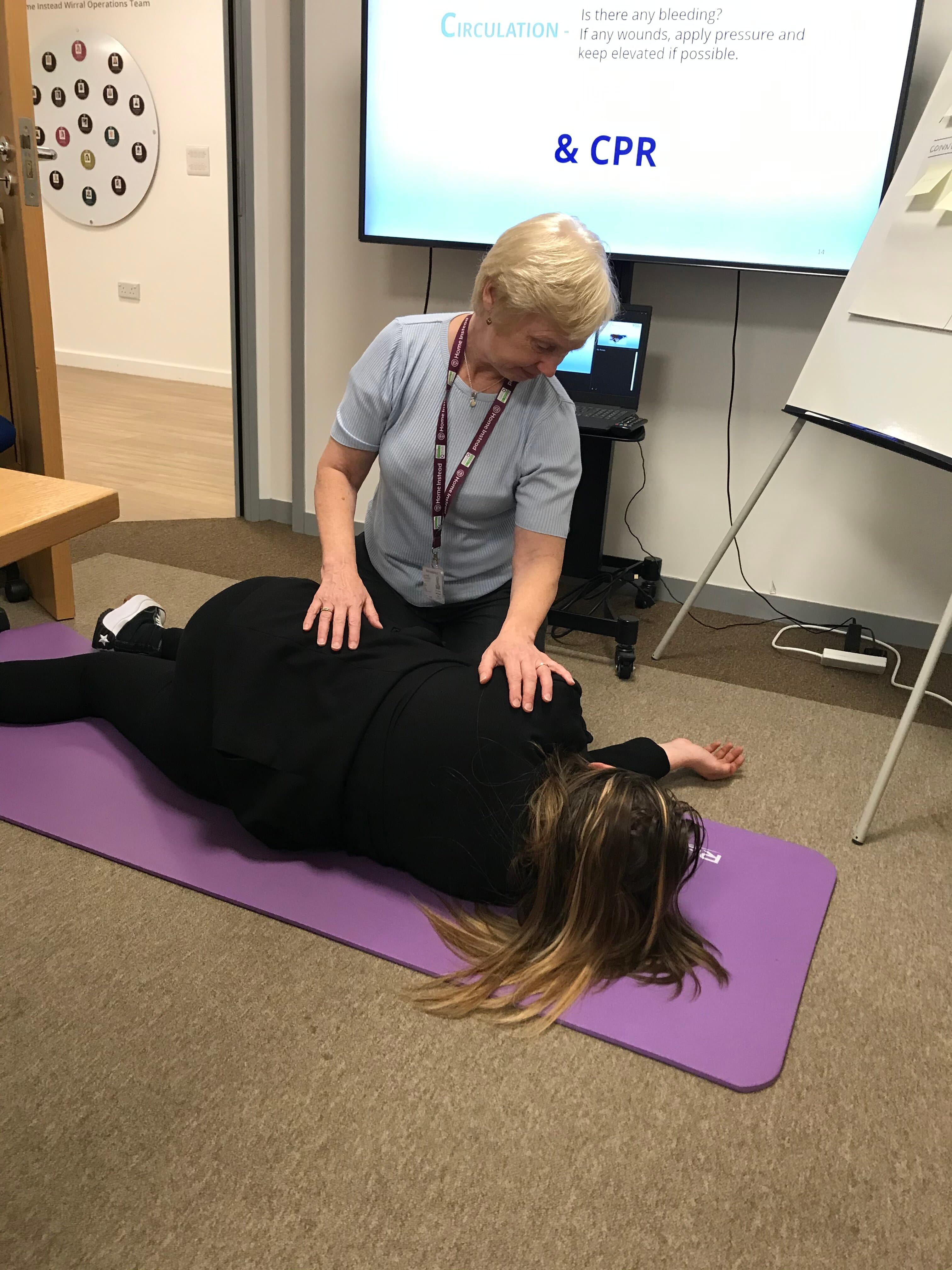 Person demonstrating CPR technique on a participant lying on a mat during a CPR training session. - Home Instead