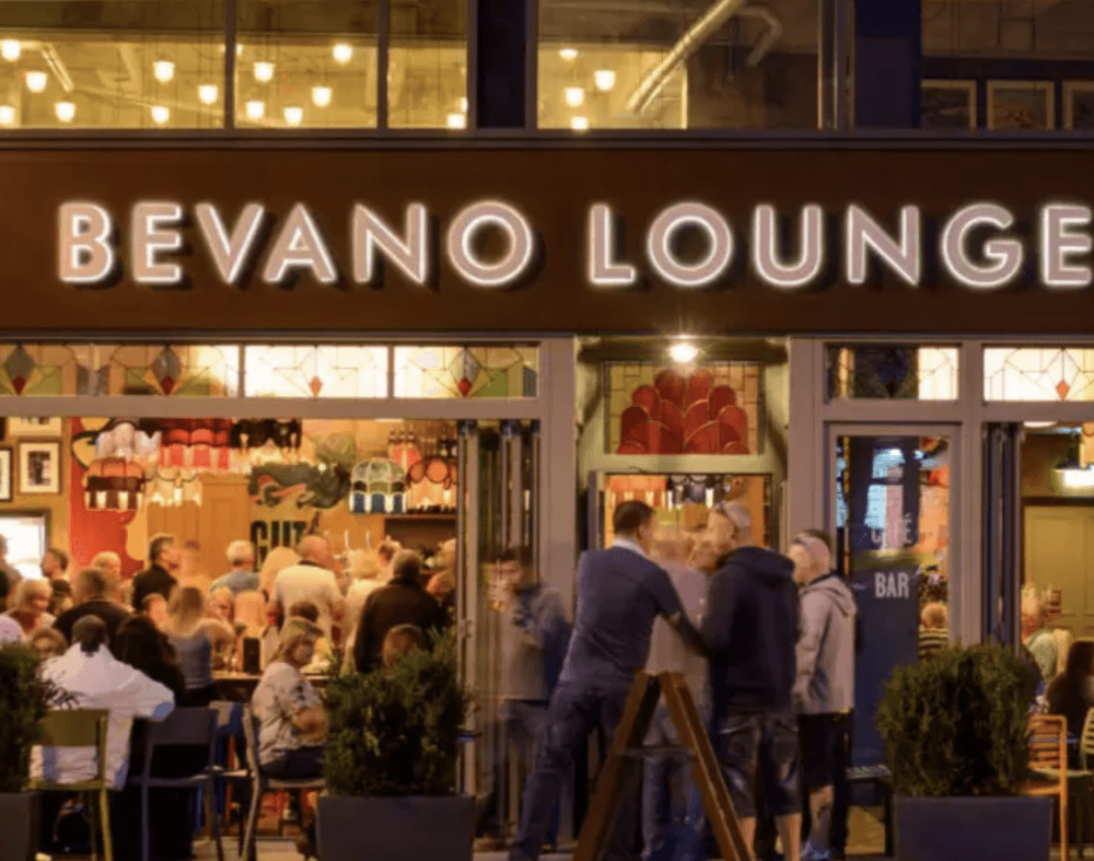A bustling evening scene at Bevano Lounge, with people socializing inside and outside the well-lit bar. - Home Instead