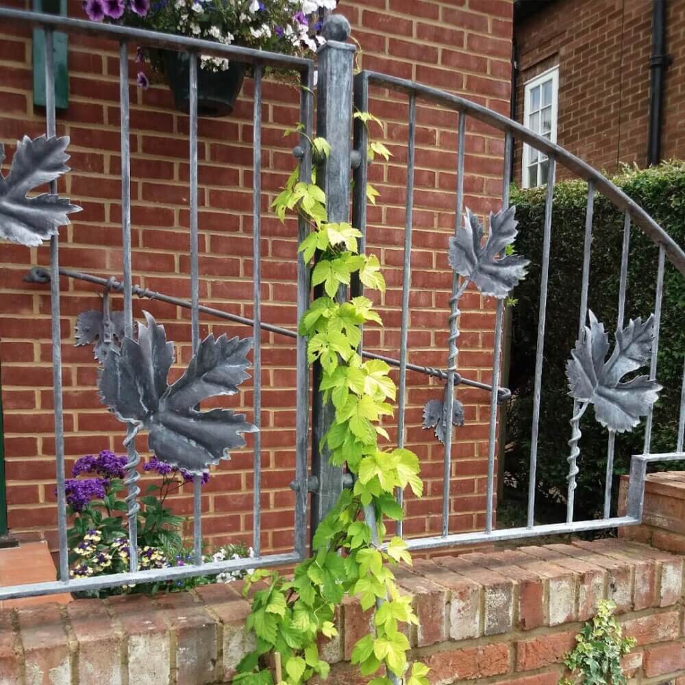 Wrought iron gate with leaf designs and climbing green vine, in front of a brick house with window and flower pot. - Home Instead