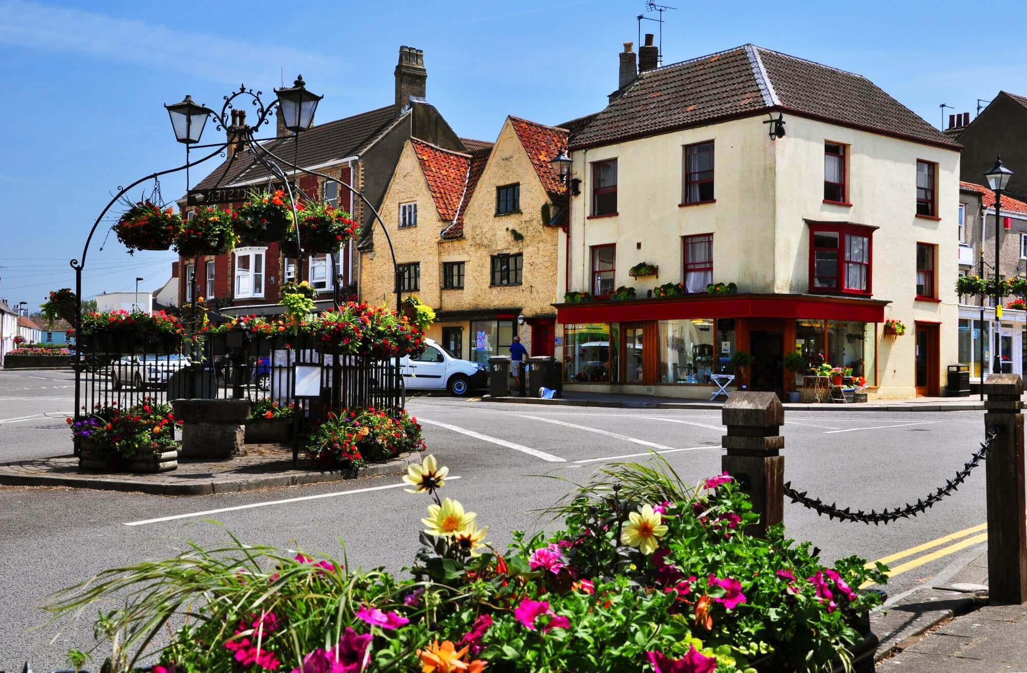 A quaint town square with historic buildings, a vintage street lamp, and vibrant flower arrangements in planters. - Home Instead