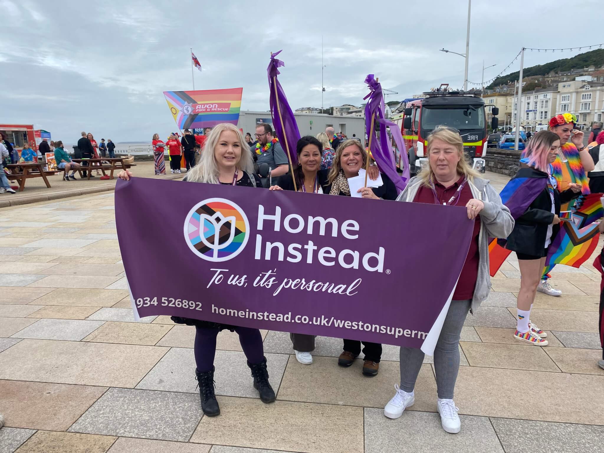 A group of people holding a "Home Instead" banner at an outdoor event. - Home Instead