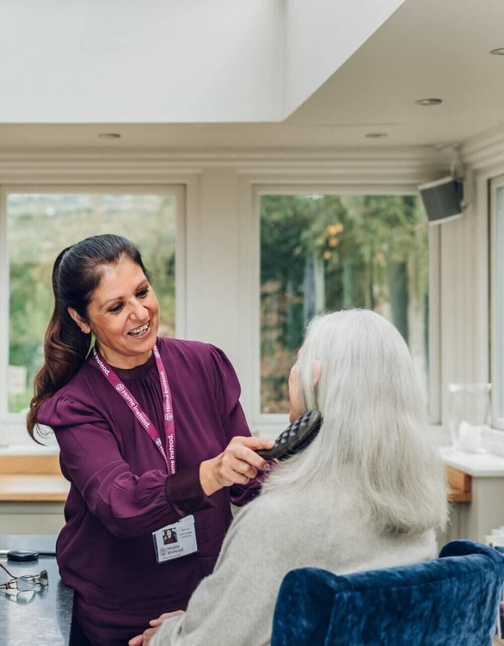 A healthcare worker smiling and examining an elderly man's ear with an otoscope in a medical setting. - Home Instead