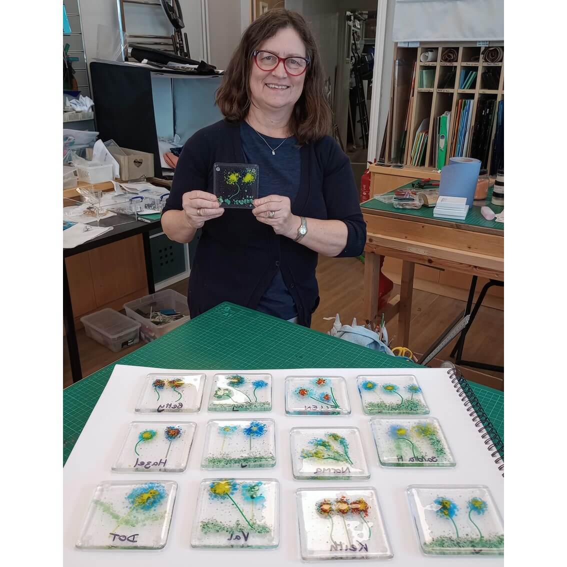 Person holding art piece in studio, with multiple similar pieces displayed on a table in front of them. - Home Instead