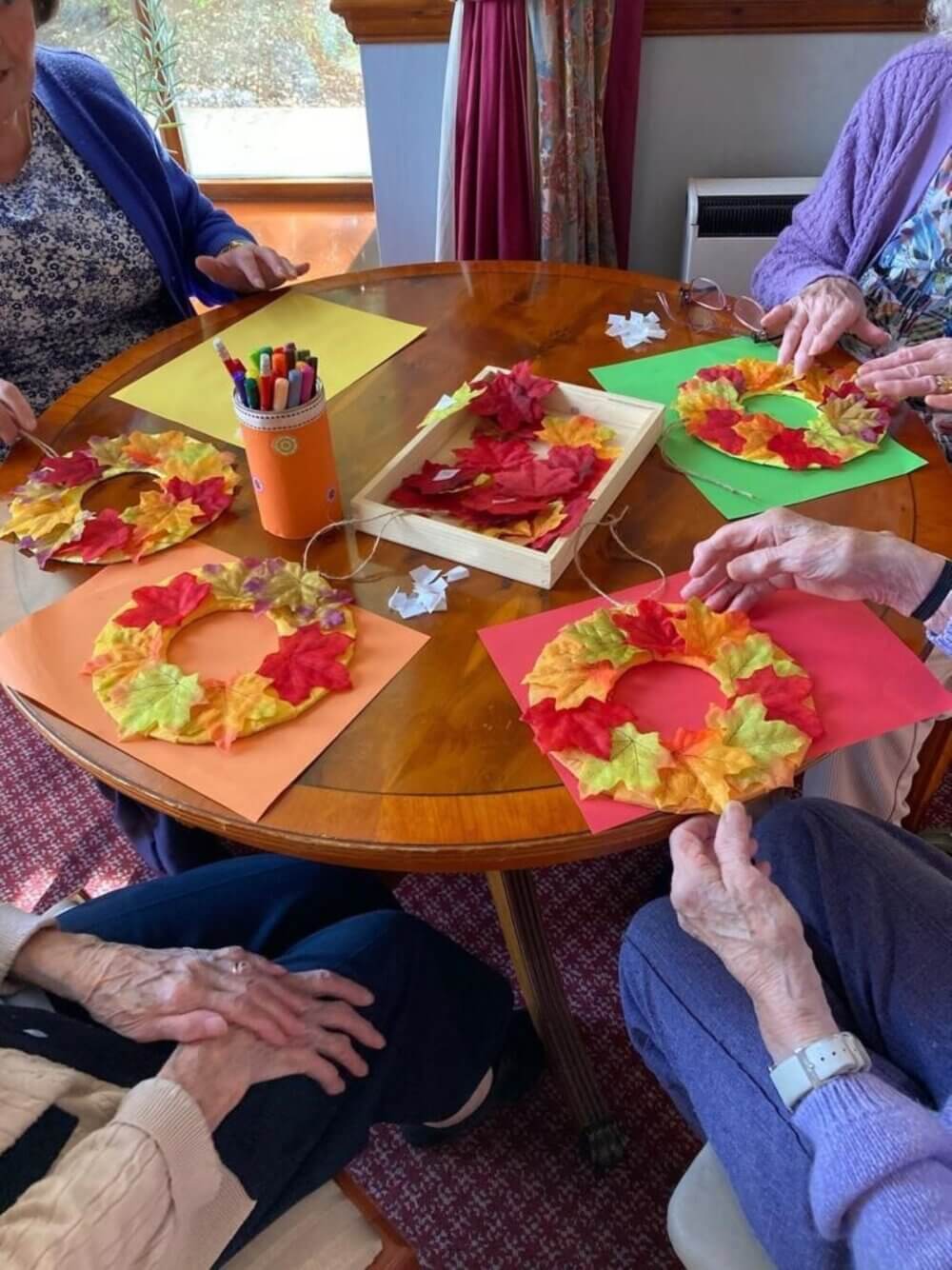 People crafting autumn wreaths with colorful leaves at a round table. - Home Instead