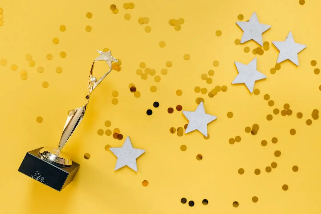 Golden trophy with star topper on black base and scattered stars and confetti on a yellow background. - Home Instead