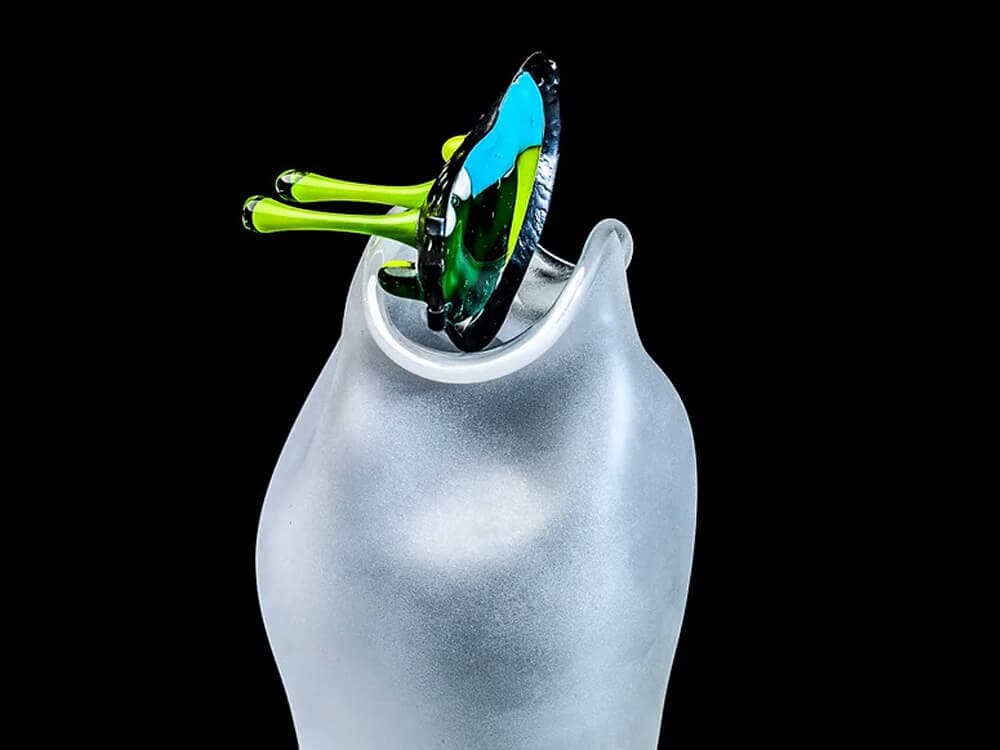 A frosted glass vase with an abstract green and blue glass arrangement extending from its top against a black background. - Home Instead
