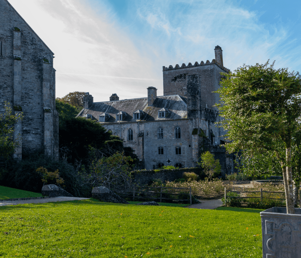 Historic stone castle with turrets and ivy-covered walls, surrounded by greenery and against a blue sky. - Home Instead
