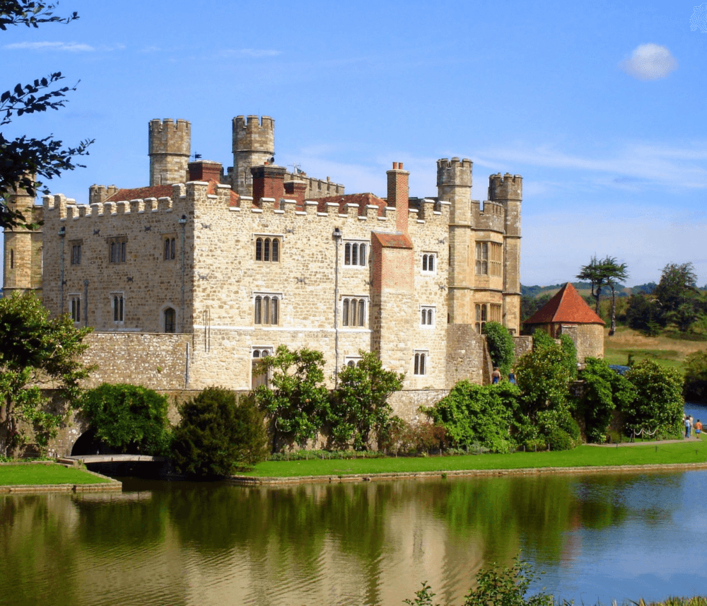 Medieval castle with towers and crenellations, surrounded by a moat, with greenery and clear blue skies in the background. - Home Instead